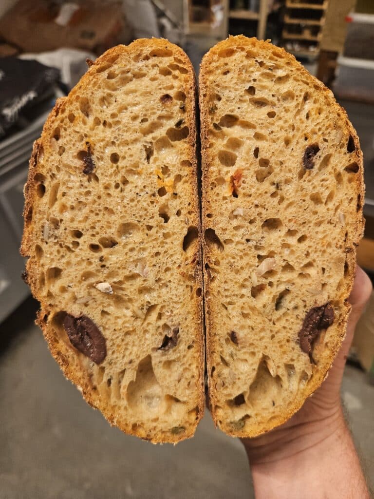 Een opgesneden borrelbrood gevuld met kappertjes, zongedroogde tomaten, zonnebloempitten en olijven.